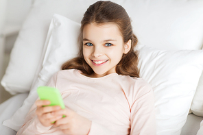 people, children, rest and technology concept - happy smiling girl lying awake with smartphone in bed at home