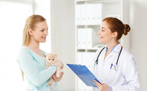 medicine, pet, animals, health care and people concept - happy woman holding scottish fold kitten and veterinarian doctor with clipboard at vet clinic