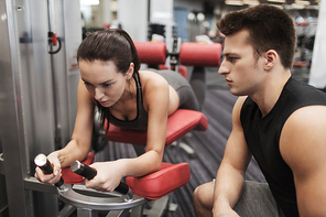 sport, fitness, lifestyle and people concept - young woman and personal trainer flexing leg muscles on gym machine