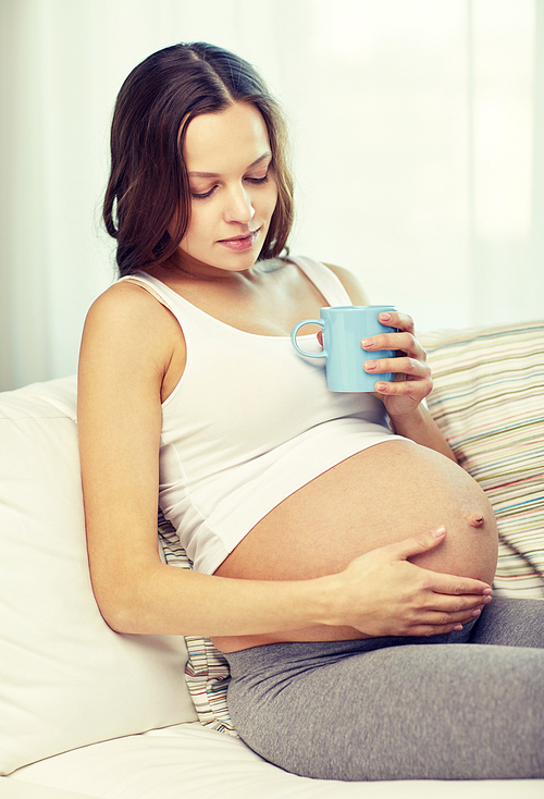 pregnancy, drinks, rest, people and expectation concept - happy pregnant woman with cup drinking tea at home