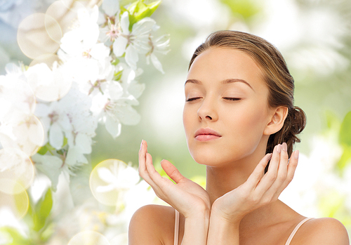 beauty, people, skincare, summer and health concept - young woman face and hands over green natural background with cherry blossom