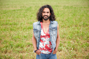 nature, summer, youth culture and people concept - smiling young hippie man in denim vest on green field