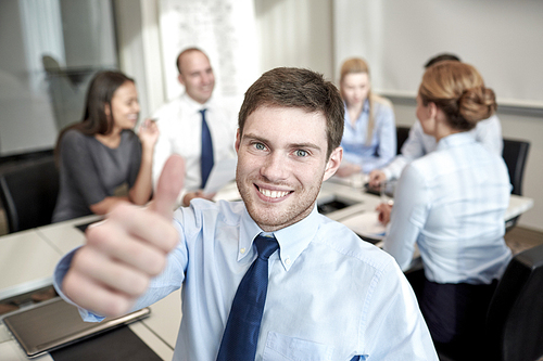 business, people, gesture and teamwork concept - smiling businessman showing thumbs up with group of businesspeople meeting in office