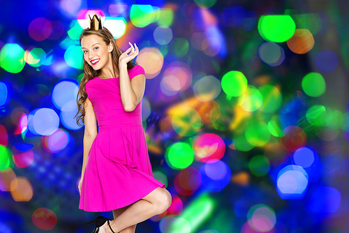 people, holidays and fashion concept - happy young woman or teen girl in pink dress and princess crown over holidays lights background