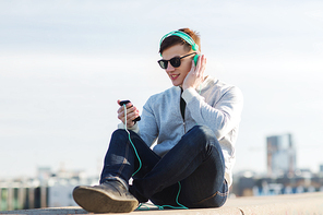 technology, lifestyle and people concept - smiling young man or teenage boy in headphones with smartphone listening to music outdoors