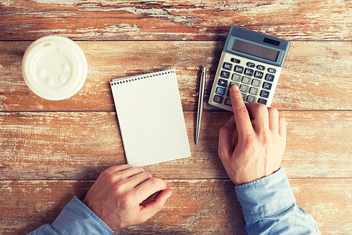 business, education, people and technology concept - close up of male hands with calculator, pen and notebook on table