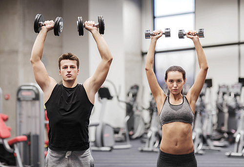 sport, fitness, lifestyle and people concept - smiling man and woman with dumbbells flexing muscles in gym