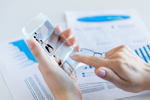 business, technology, news, mass media and people concept - close up of woman hand holding transparent smartphone with web page on screen at office