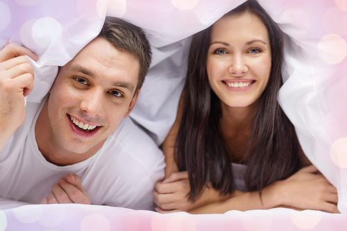 love, valentines day and people concept - happy couple in bed over holidays lights background