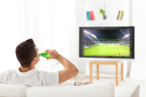 leisure, technology, sport, alcohol and people concept - man drinking beer and watching football game on tv at home from back