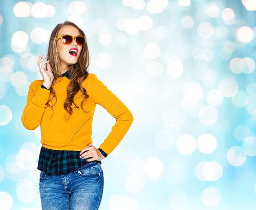 people, style and fashion concept - happy young woman or teen girl in casual clothes and sunglasses over blue lights background