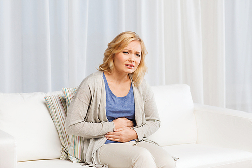 people, healthcare and problem concept - unhappy woman suffering from stomach ache at home