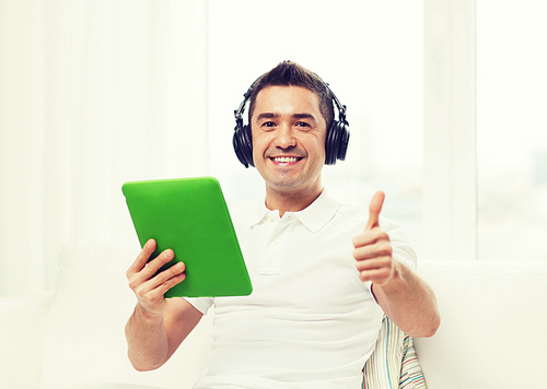 technology, people, lifestyle and distance learning concept - happy man with tablet pc computer and headphones listening to music and showing thumbs up at home