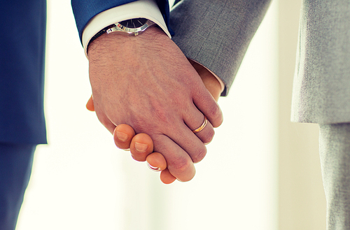 people, homosexuality, same-sex marriage and love concept - close up of happy male gay couple holding hands with wedding rings on