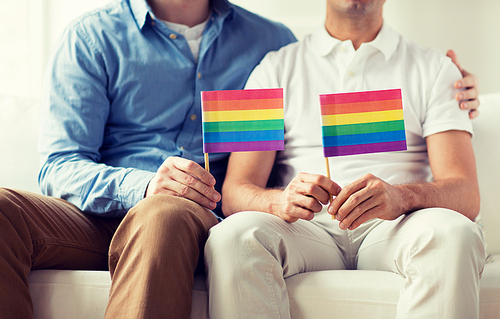 people, homosexuality, same-sex marriage, gay and love concept - close up of happy male gay couple hugging and holding rainbow flags at home