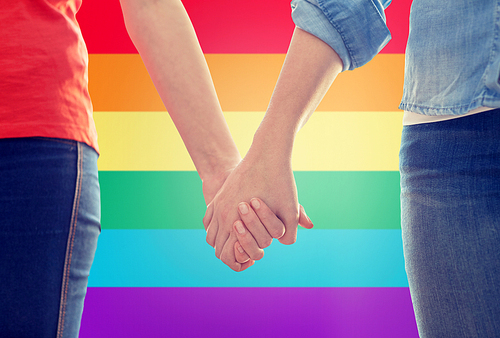 people, homosexuality, same-sex marriage, gay and love concept - close up of happy lesbian couple holding hands over rainbow flag background