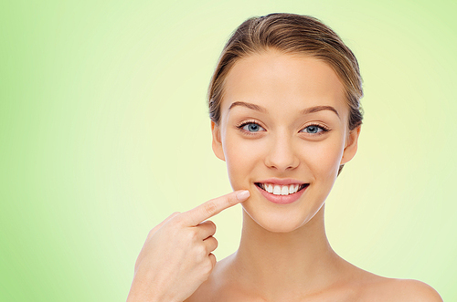 beauty, people, dental care and hygiene concept - happy young woman pointing finger to her smile or teeth over green background