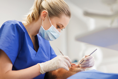 people, medicine, stomatology and health care concept - female dentist with dental mirror and probe checking up male patient teeth at dental clinic office