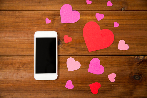 advertisement, romance, valentines day and holidays concept - close up of smartphone and hearts on wood