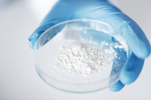 science, chemistry, biology, medicine and people concept - close up of scientist hand holding petri dish with powder in clinical laboratory