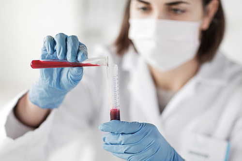 science, chemistry, biology, medicine and people concept - close up of young female scientist holding tube with blood sample making and test or research in clinical laboratory