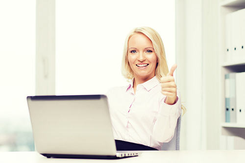 education, business and technology concept - smiling businesswoman or student showing thumbs up with laptop computer in office