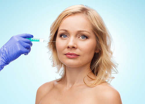 beauty, anti-aging cosmetic surgery concept - middle aged woman face and beautician hand in glove with syringe making injection to cheek over blue background