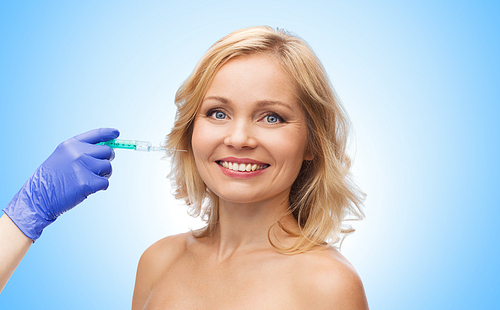 beauty, anti-aging cosmetic surgery concept - smiling middle aged woman face and beautician hand in glove with syringe making injection to cheek over blue background