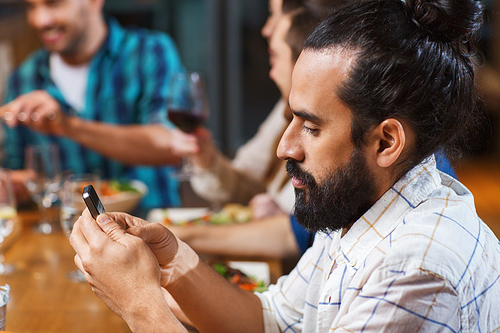 leisure, technology, internet addiction, lifestyle and people concept - man with smartphone and friends at restaurant