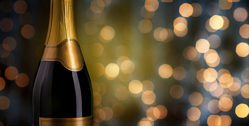 drink, alcohol, advertisement and holidays concept - close up of bottle of champagne with blank golden label over lights background