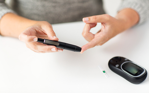 medicine, diabetes, glycemia, health care and people concept - close up of woman checking blood sugar level by glucometer at home