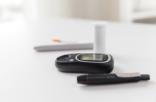 medicine, diabetes and health care concept - close up of glucometer and blood sugar test stick on table
