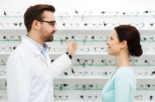 health care, people, eyesight and vision concept - optician showing glasses to woman at optics store