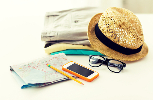 travel, summer vacation, tourism and objects concept - close up of folded clothes, smartphone and touristic map on table at home