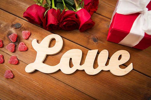 romance, valentines day and holidays concept - close up of word love, gift box, red roses and heart-shaped candies on wood