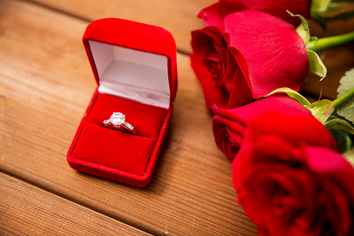 love, proposal, valentines day and holidays concept - close up of gift box with diamond engagement ring and red roses on wood