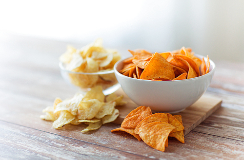 fast food, junk-food, cuisine and unhealthy eating concept - close up of crunchy potato crisps and corn crisps or nachos in bowls