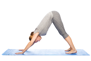 fitness, sport, people and healthy lifestyle concept - woman making yoga in downward facing dog pose on mat