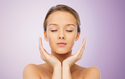 beauty, people, skincare and health concept - young woman face and hands over violet background