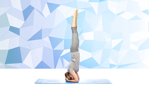 fitness, sport, people and healthy lifestyle concept - woman making yoga in headstand pose on mat over blue polygonal background