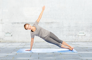 fitness, sport, people and healthy lifestyle concept - woman making yoga in side plank pose on mat over urban street background