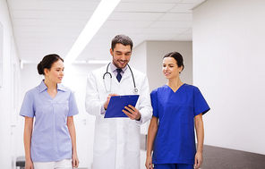 clinic, profession, people, health care and medicine concept - group of smiling medics or doctors with clipboard walking along hospital corridor