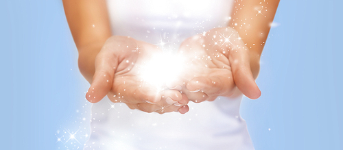 people and magic concept - close up of twinkles or fairy dust on female cupped hands over blue background