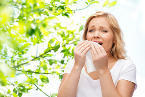 people, healthcare, rhinitis and allergy concept - unhappy woman with paper napkin sneezing over green natural background