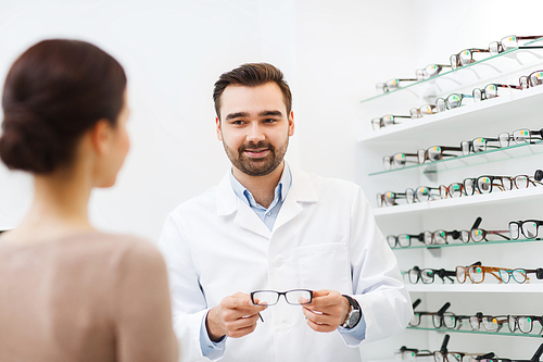 health care, people, eyesight and vision concept - optician showing glasses to woman at optics store