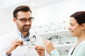 health care, people, eyesight and vision concept - optician showing glasses to woman at optics store
