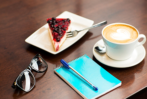 lifestyle and object concept - close up of notebook with pen, eyeglasses, coffee cup and berry cake on table