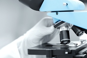 science, chemistry, biology, medicine and people concept - close up of scientist hand in glove setting microscope and making research in clinical laboratory