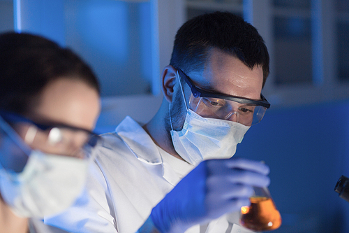 science, chemistry, biology, medicine and people concept - close up of young scientists with pipette and flasks making test or research in clinical laboratory