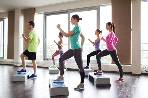 fitness, sport, training, aerobics and people concept - group of people working out with steppers in gym